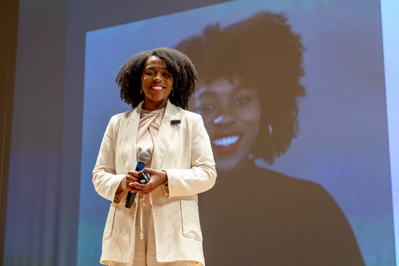 Kizzy Terra sorrindo no palco, com microfone na mão