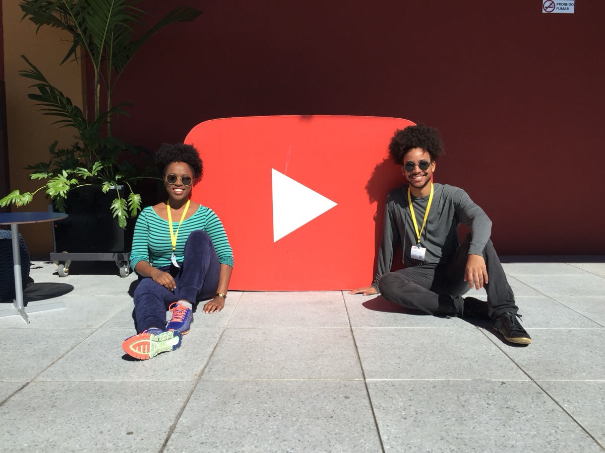 Kizzy Terra e Hallison Paz sentados em frente ao logo do YouTube na sede da empresa.